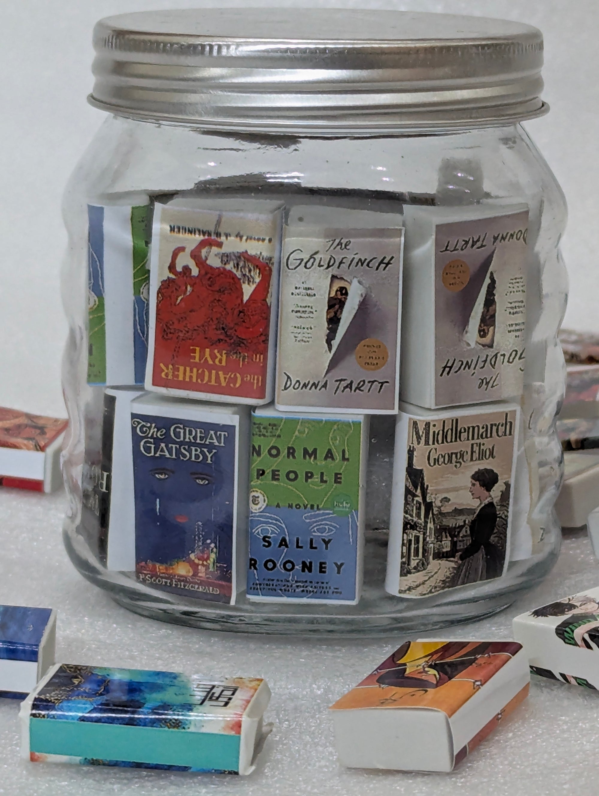 Glass jar filled with miniature books on a white surface