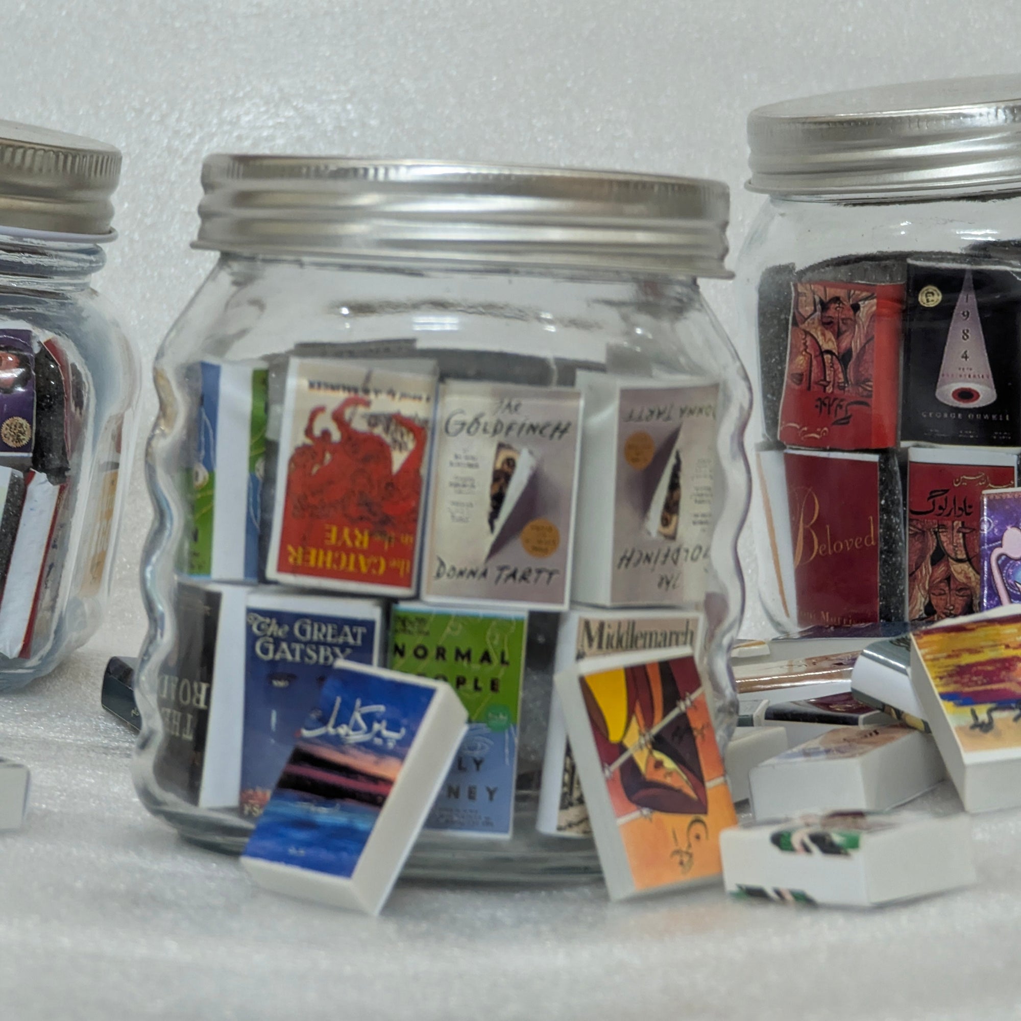 Glass jars filled with miniature books on a white surface